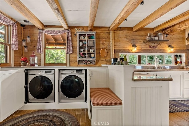 clothes washing area with hardwood / wood-style flooring, a wealth of natural light, washer and clothes dryer, and wood walls