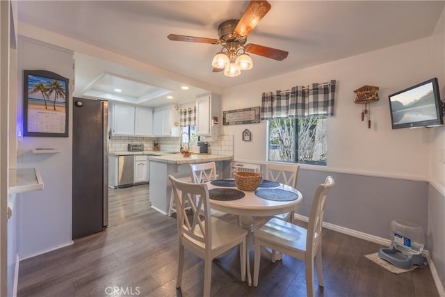 dining space featuring ceiling fan, dark hardwood / wood-style flooring, sink, and a raised ceiling