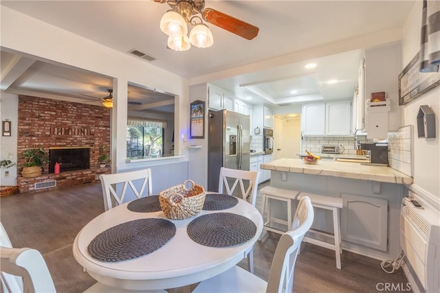 dining room with ceiling fan, a wall mounted AC, a fireplace, dark hardwood / wood-style floors, and a raised ceiling