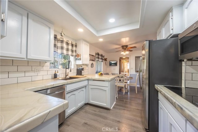 kitchen featuring a raised ceiling, kitchen peninsula, sink, white cabinetry, and light hardwood / wood-style flooring