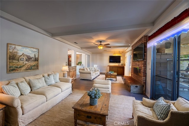 living room featuring ceiling fan, wood-type flooring, a brick fireplace, and beamed ceiling