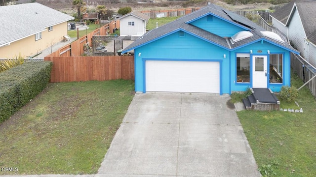 view of front facade with a fenced backyard, solar panels, an attached garage, and a front yard