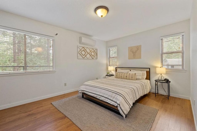 bedroom featuring multiple windows, a wall mounted air conditioner, and hardwood / wood-style flooring