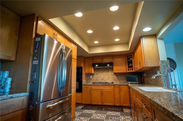 kitchen with a raised ceiling, sink, backsplash, black appliances, and light stone countertops