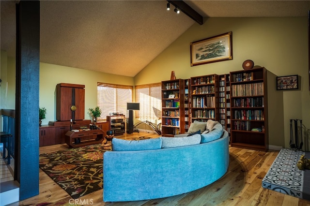 living room with light wood-type flooring, vaulted ceiling with beams, and a textured ceiling