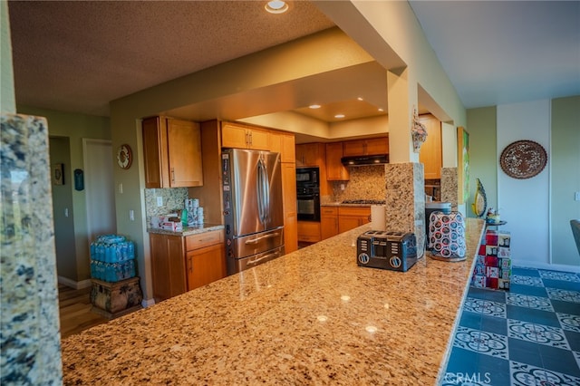 kitchen featuring light stone counters, a textured ceiling, kitchen peninsula, black appliances, and backsplash