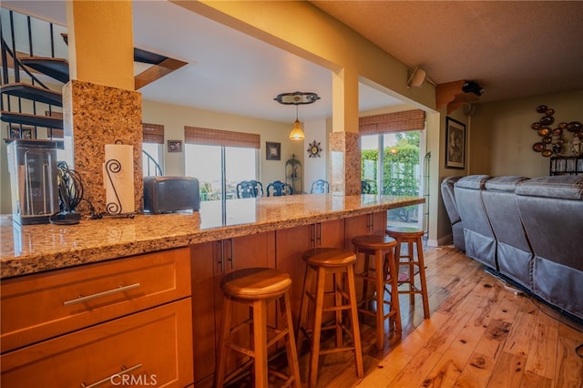 kitchen featuring a wealth of natural light, light wood-type flooring, hanging light fixtures, and a breakfast bar