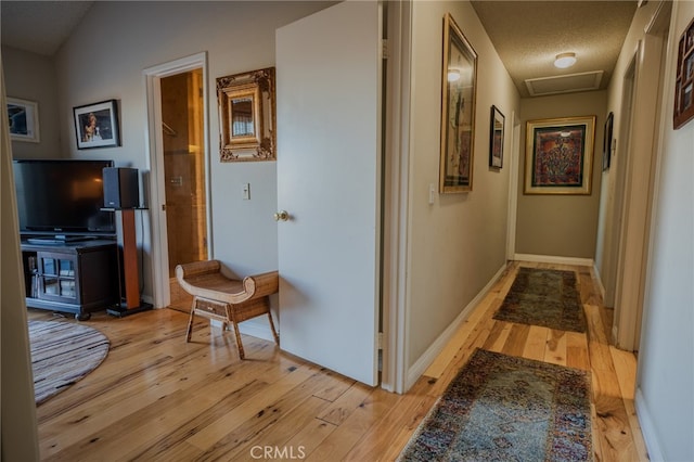 corridor with a textured ceiling and light hardwood / wood-style floors