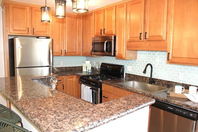 kitchen with decorative backsplash, stainless steel appliances, sink, dark stone countertops, and hanging light fixtures