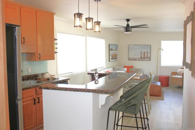 kitchen featuring ceiling fan, stainless steel fridge, light hardwood / wood-style floors, decorative backsplash, and ornamental molding