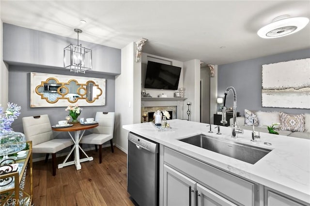 kitchen featuring dark wood-type flooring, sink, light stone counters, hanging light fixtures, and stainless steel dishwasher