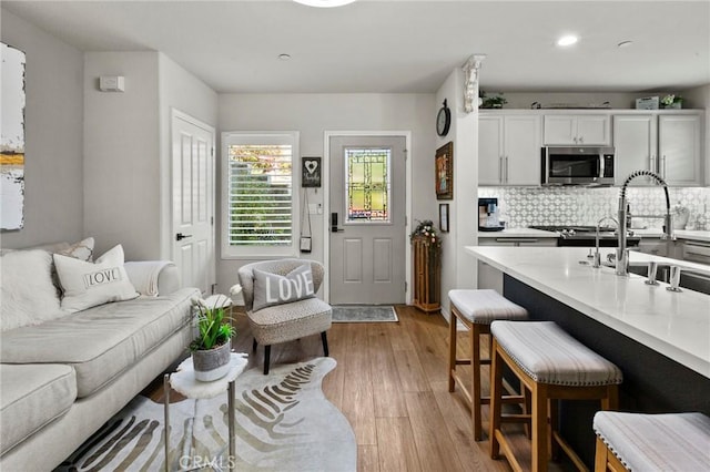 kitchen featuring sink, a breakfast bar area, light wood-type flooring, white cabinets, and backsplash