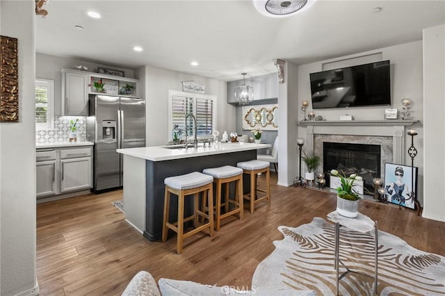 kitchen featuring gray cabinetry, a center island with sink, stainless steel fridge, pendant lighting, and a high end fireplace