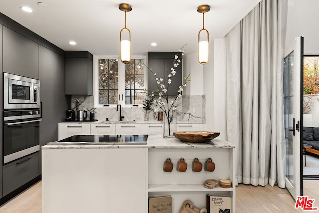 kitchen featuring stainless steel appliances, decorative light fixtures, sink, and light stone counters