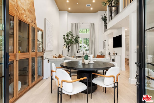 dining room with light wood-type flooring and a towering ceiling