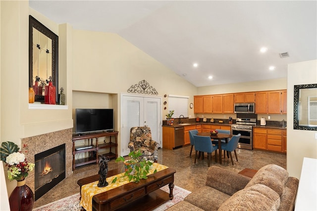 living area with high vaulted ceiling, a glass covered fireplace, visible vents, and recessed lighting