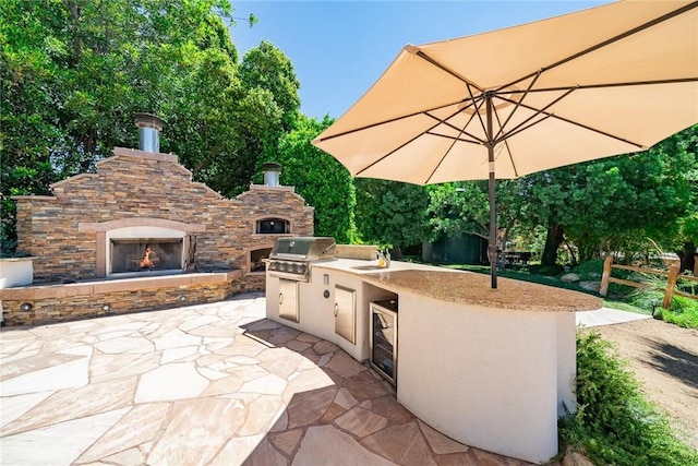 view of patio featuring an outdoor stone fireplace, an outdoor kitchen, beverage cooler, and a grill