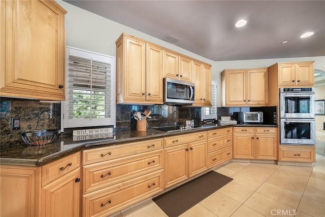 kitchen with dark stone counters, decorative backsplash, light tile patterned floors, light brown cabinetry, and appliances with stainless steel finishes