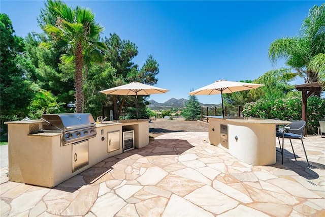 view of patio featuring an outdoor wet bar, exterior kitchen, grilling area, a mountain view, and wine cooler