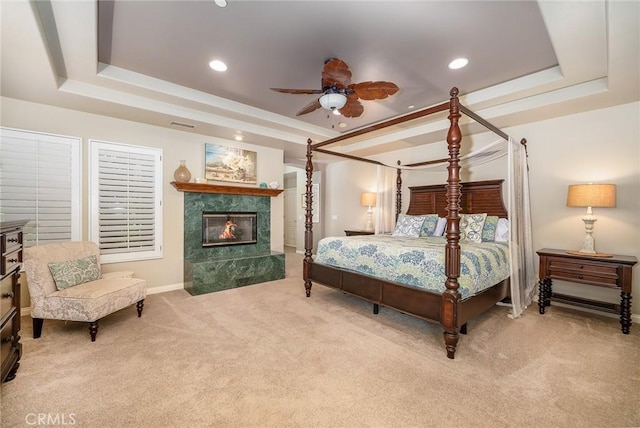 carpeted bedroom with ceiling fan, a raised ceiling, and a fireplace