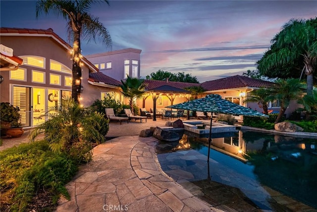 pool at dusk featuring a patio area and an in ground hot tub