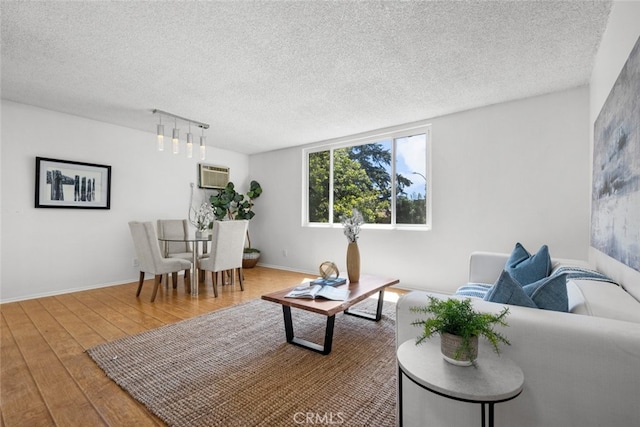 living room featuring a wall mounted AC, hardwood / wood-style flooring, and a textured ceiling