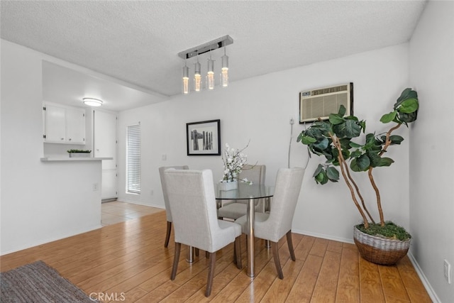 dining area featuring a wall mounted air conditioner, light hardwood / wood-style flooring, and a textured ceiling