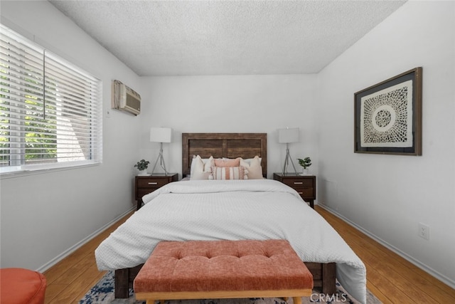 bedroom with light hardwood / wood-style flooring, a textured ceiling, and a wall mounted AC