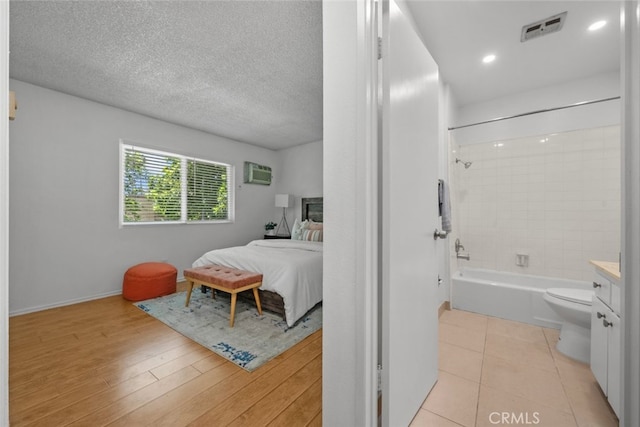 bedroom featuring a wall mounted air conditioner, light hardwood / wood-style flooring, and a textured ceiling