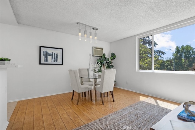 dining space with an AC wall unit, a textured ceiling, and light hardwood / wood-style flooring