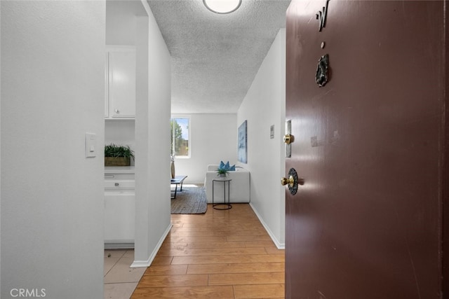 hallway with a textured ceiling and light wood-type flooring