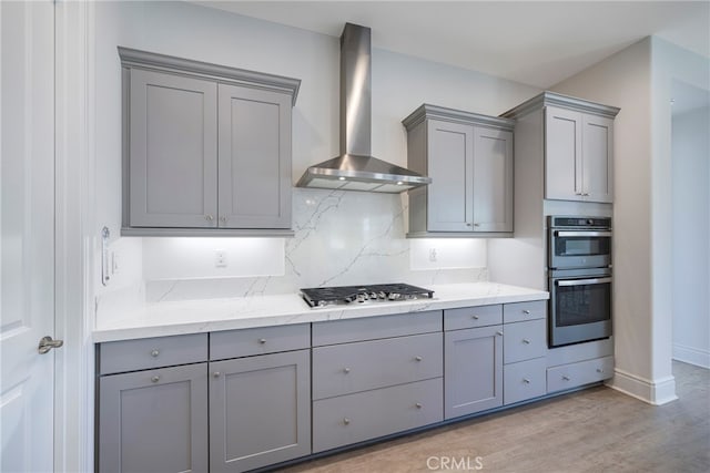 kitchen with gray cabinetry, light wood-type flooring, appliances with stainless steel finishes, and wall chimney range hood