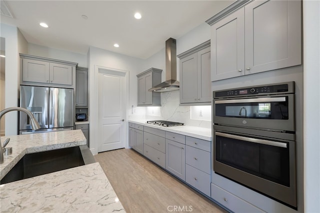 kitchen featuring sink, wall chimney exhaust hood, gray cabinets, appliances with stainless steel finishes, and light wood-type flooring