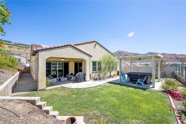 rear view of property featuring a yard, a mountain view, ceiling fan, a patio area, and a hot tub