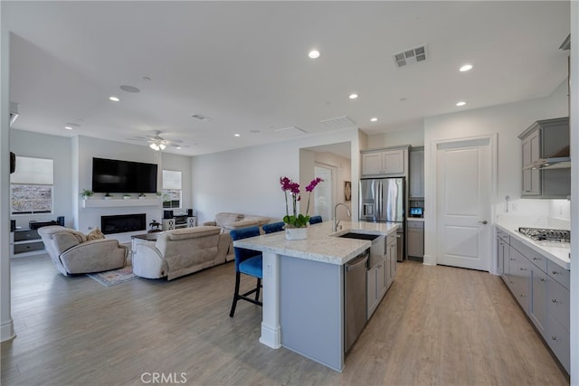 kitchen featuring ceiling fan, an island with sink, light wood-type flooring, and gray cabinets