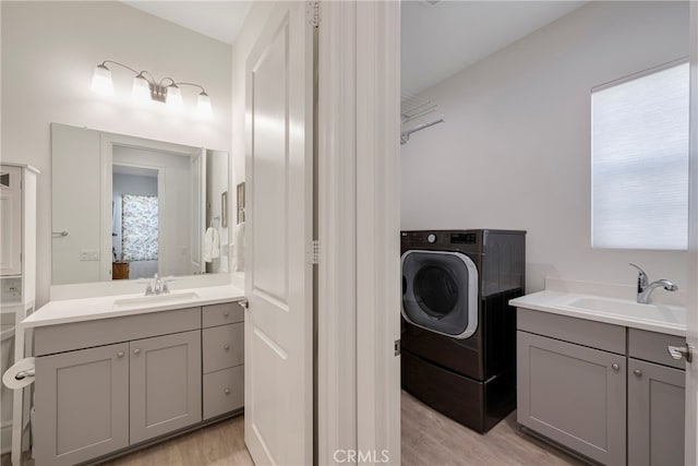 clothes washing area with washer / clothes dryer, light hardwood / wood-style floors, and sink