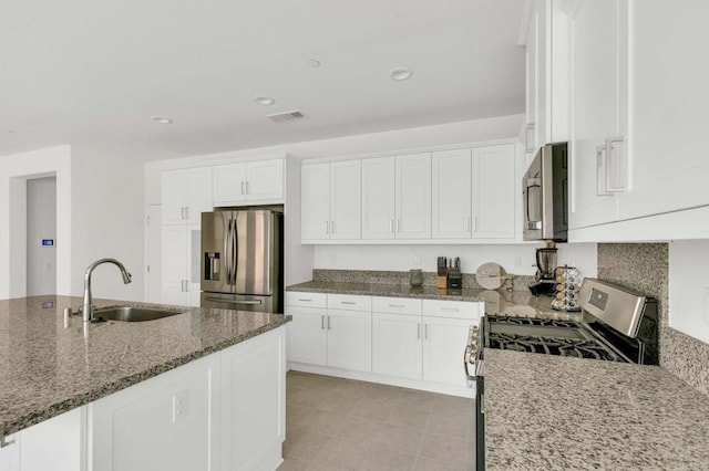 kitchen featuring white cabinets, sink, stone counters, stainless steel appliances, and decorative backsplash