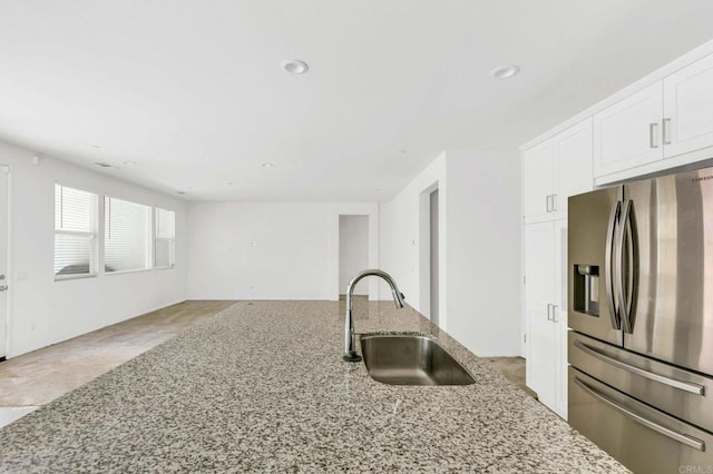 kitchen with light stone counters, stainless steel fridge, sink, and white cabinetry