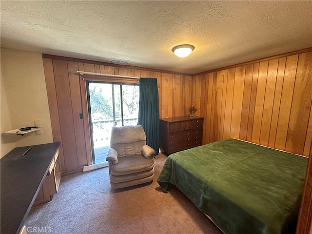 carpeted bedroom with a textured ceiling, wooden walls, and access to exterior