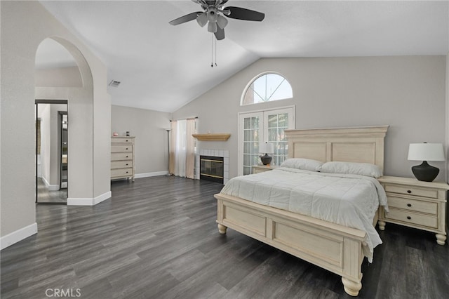 bedroom with a tiled fireplace, ceiling fan, dark wood-type flooring, and vaulted ceiling