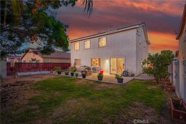 back house at dusk with a patio area and a lawn