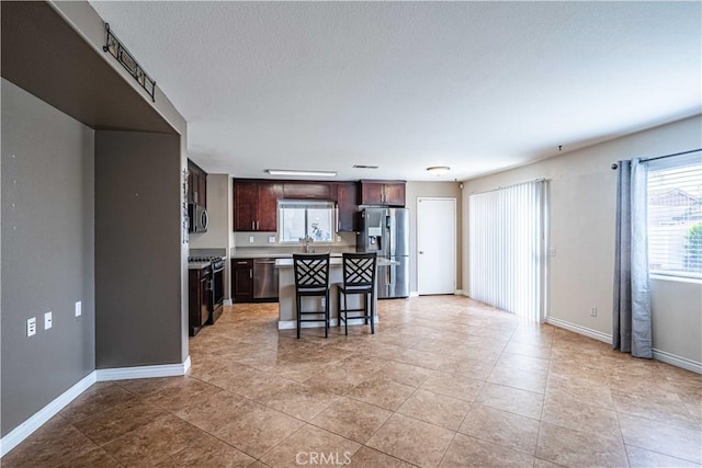 kitchen featuring a breakfast bar, appliances with stainless steel finishes, light tile patterned flooring, a kitchen island, and dark brown cabinetry