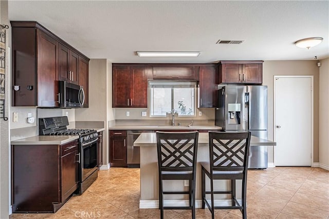 kitchen featuring light tile patterned floors, a kitchen bar, appliances with stainless steel finishes, a kitchen island, and sink