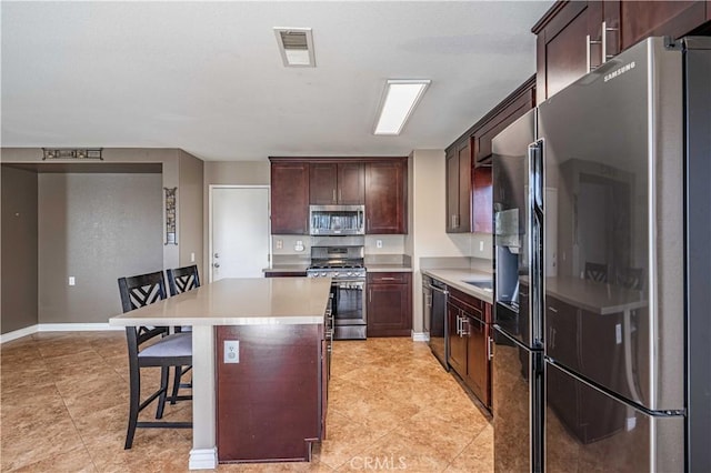 kitchen with a kitchen bar, appliances with stainless steel finishes, a center island, and dark brown cabinets