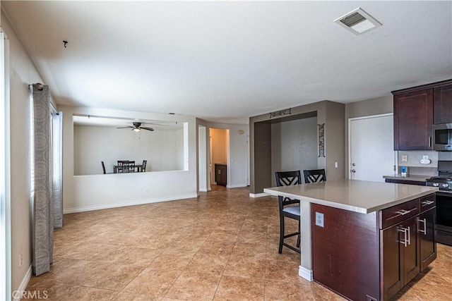 kitchen with ceiling fan, a kitchen island, a breakfast bar, stove, and dark brown cabinets