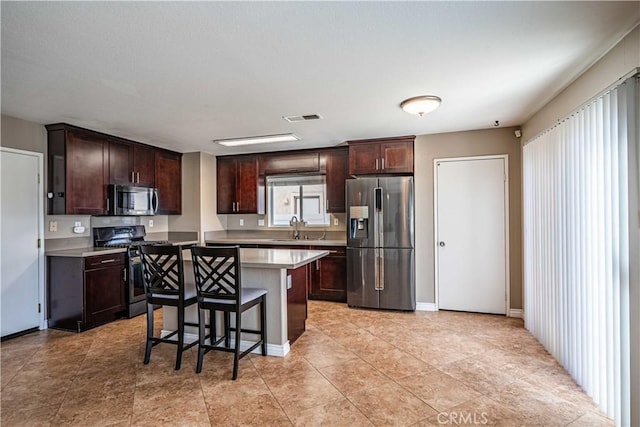 kitchen featuring a kitchen island, a kitchen bar, sink, dark brown cabinetry, and stainless steel appliances