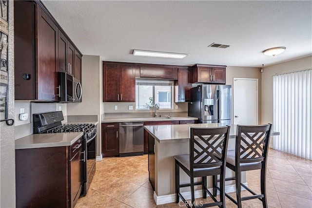 kitchen with a breakfast bar area, appliances with stainless steel finishes, a center island, light tile patterned flooring, and sink