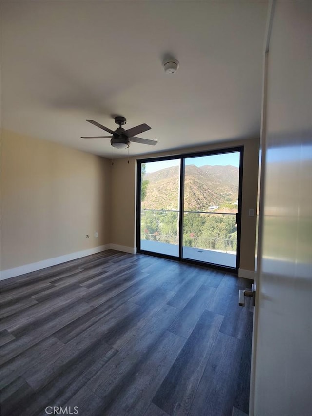 empty room featuring a mountain view, ceiling fan, and dark wood-type flooring