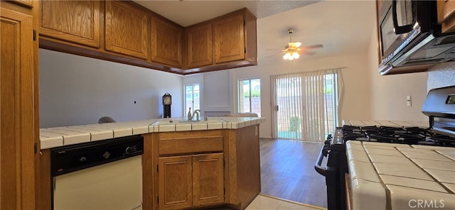 kitchen with ceiling fan, range with gas stovetop, dishwasher, tile countertops, and light hardwood / wood-style floors