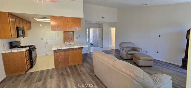 kitchen with light hardwood / wood-style floors, tile countertops, a high ceiling, and black appliances